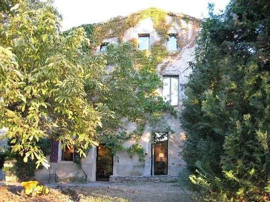 Une vieille maison en pierre entourée d'arbres, avec des fenêtres et une porte visibles, dans un environnement verdoyant.