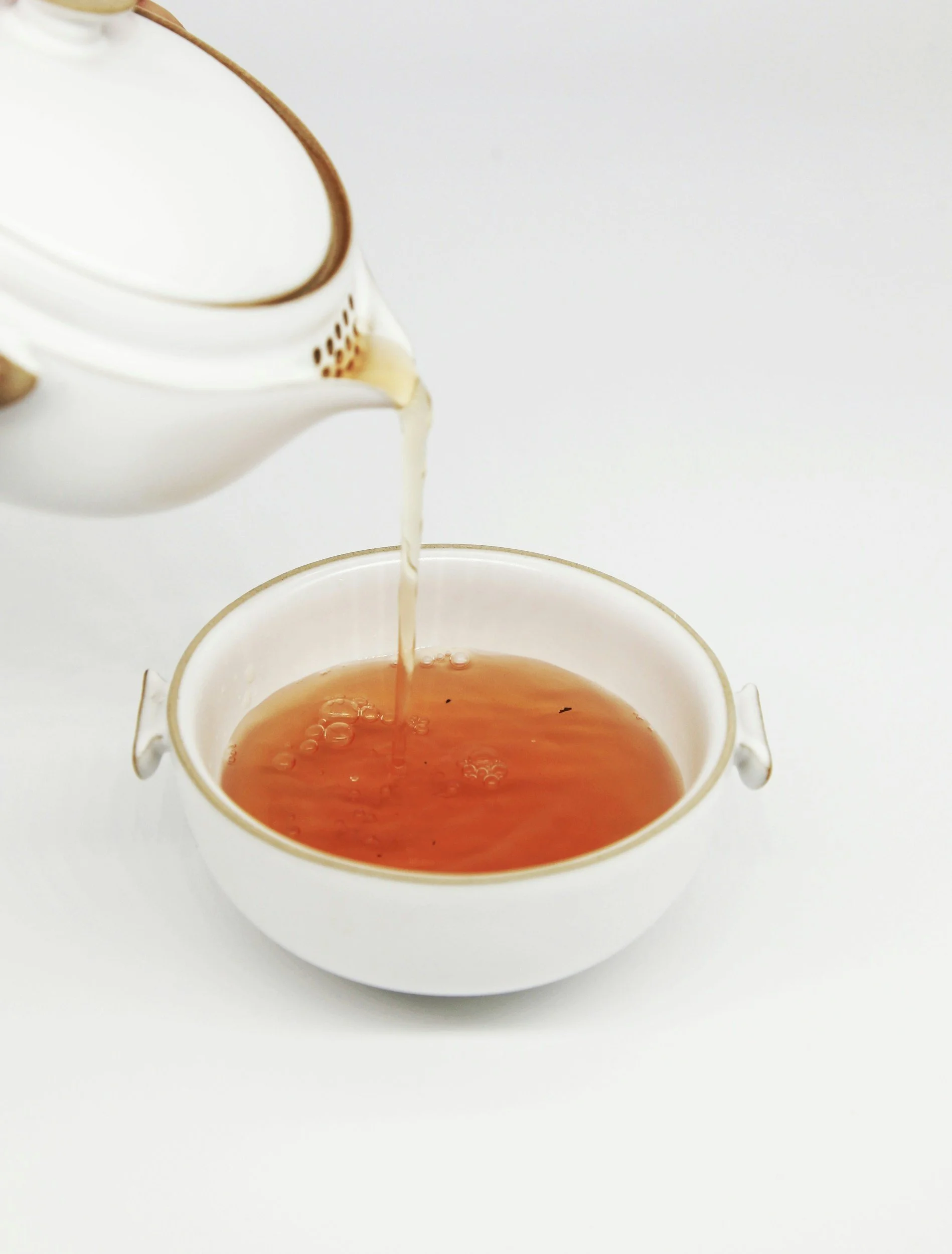 Tea being poured from a white teapot into a white teacup.