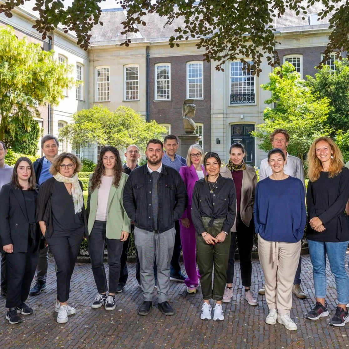 Group of diverse professionals standing outdoors in front of a historic building with greenery.