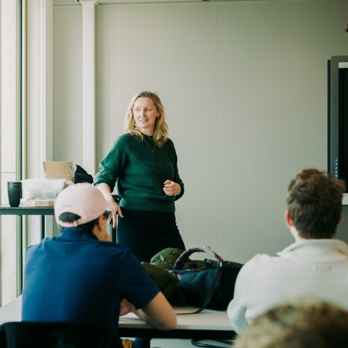 Woman giving a presentation to a group in a conference room with natural light.