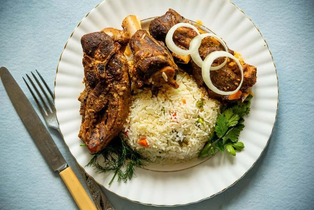 Plate of cooked rice, grilled meat, and garnished with onion slices and herbs.