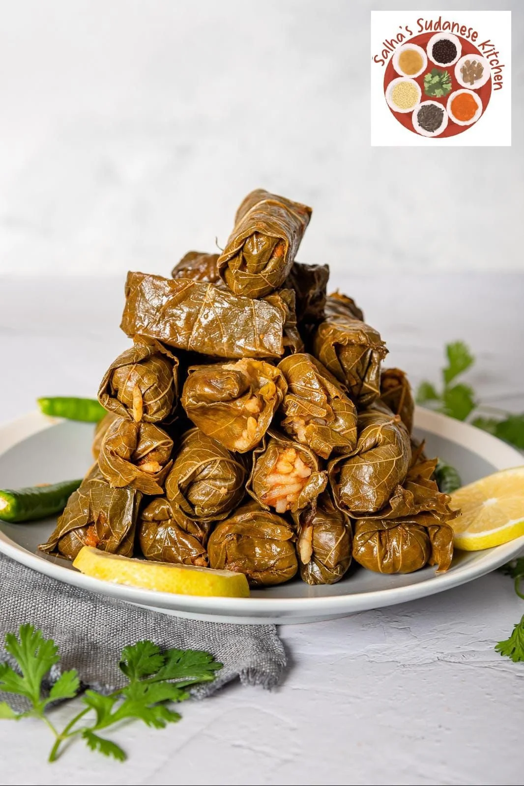 Plate of stuffed grape leaves garnished with lemon wedges, green chili peppers, and herbs.