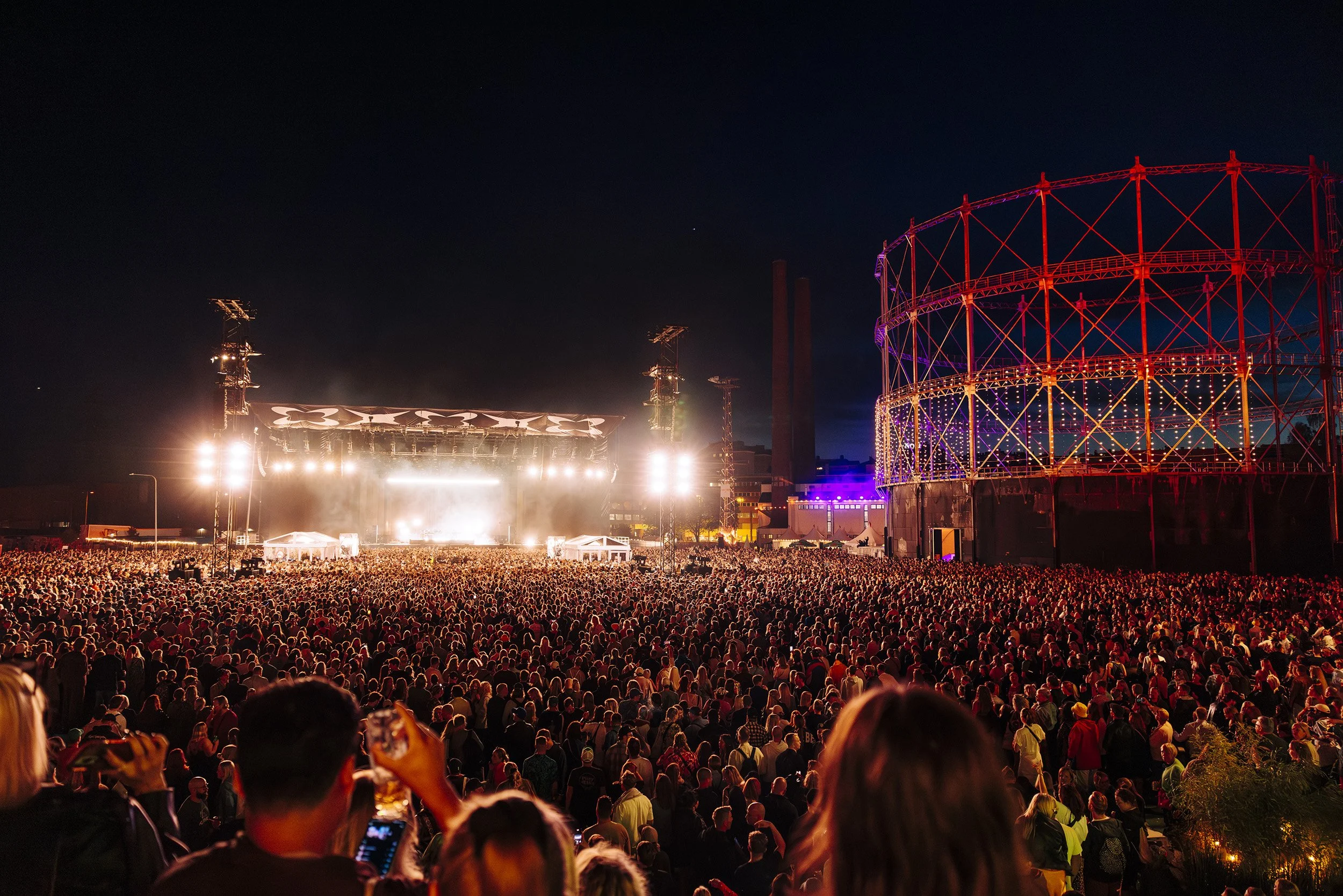 Konsertinäytös suuren ihmisjoukon edessä, kirkkaat valot ja suuri lava, ilta-aikaan.