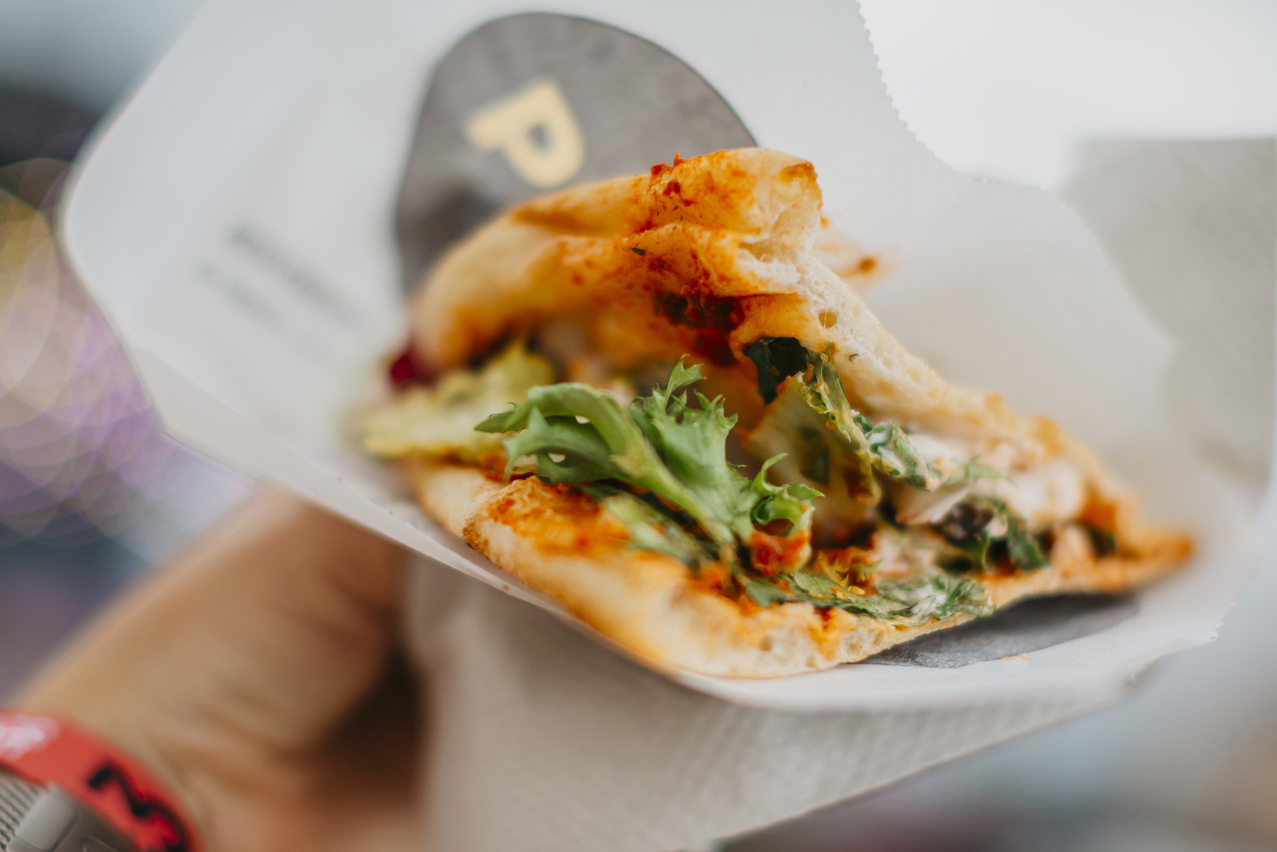 Kuvassa on pita-tyylinen leipä täytettynä vihanneksilla ja kastikkeella, osittain käärittynä paperiin.