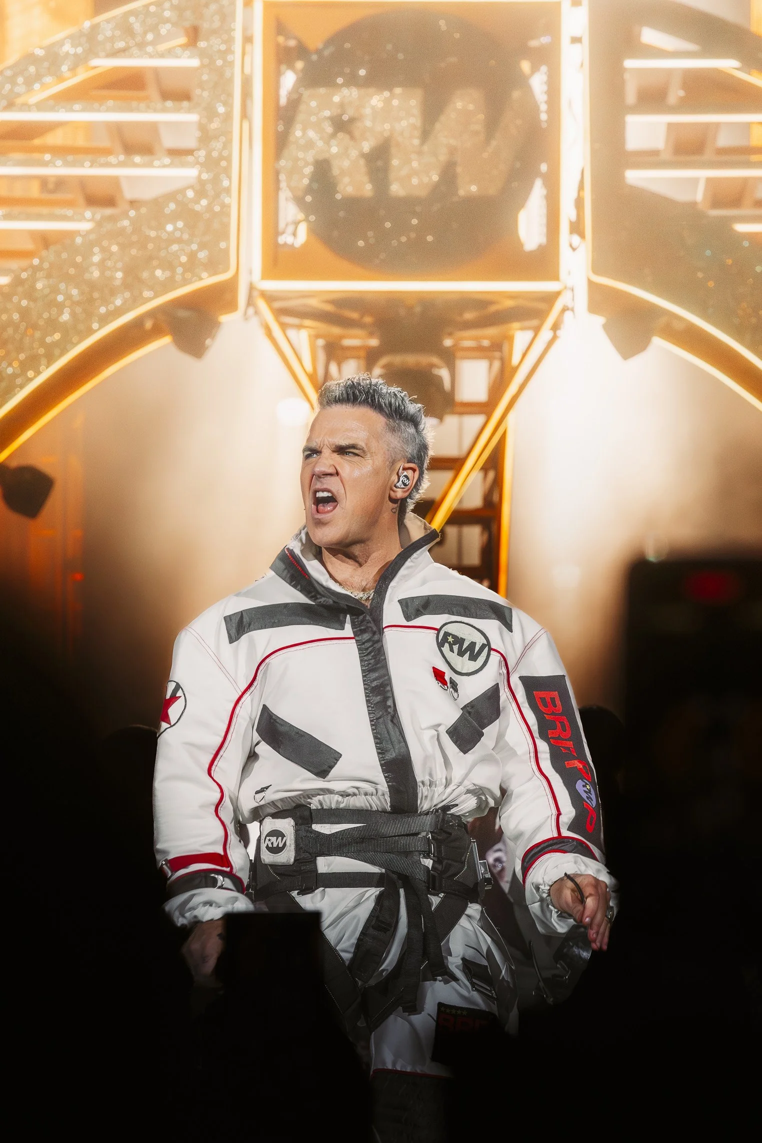 Robbie Williams esiintyy lavalla intohimoisella ilmeellä pukeutuneena valkoiseen, mustilla ja punaisilla yksityiskohdilla koristeltuun kilpa-asuun. Hänen takanaan on suuri, valaistu rakenne, jossa näkyy RW-logo ja kimaltelevia koristeita.