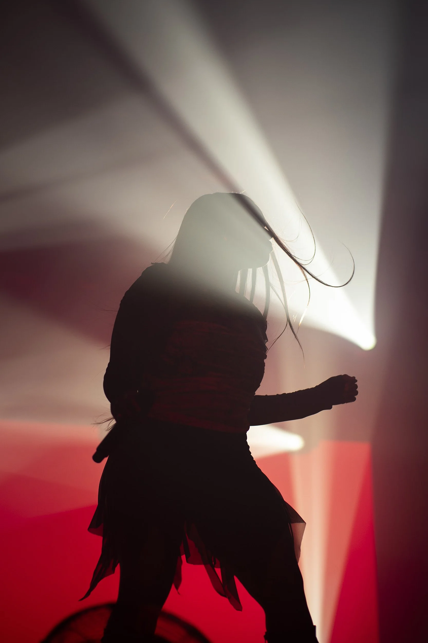 Nainen tanssimassa lavalla valojen ja savusäteiden keskellä, pimeässä.