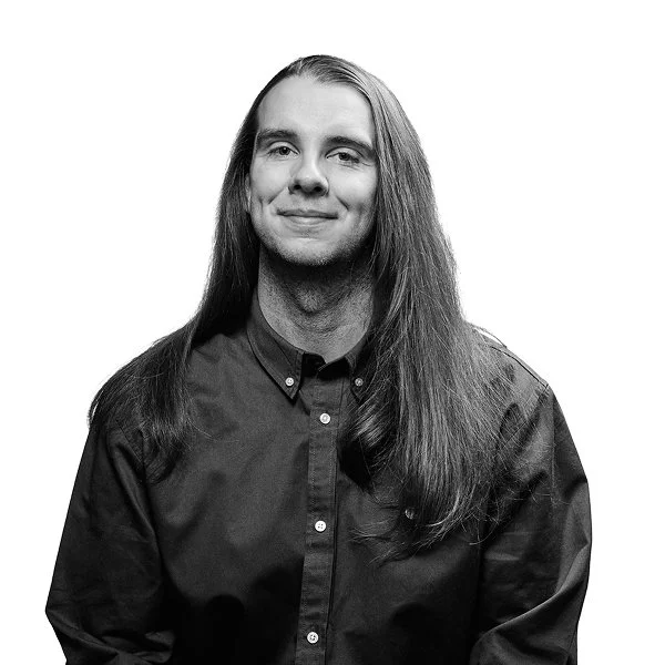 Petri Anttila, jolla pitkät hiukset, paita, hymy, valkoinen tausta.