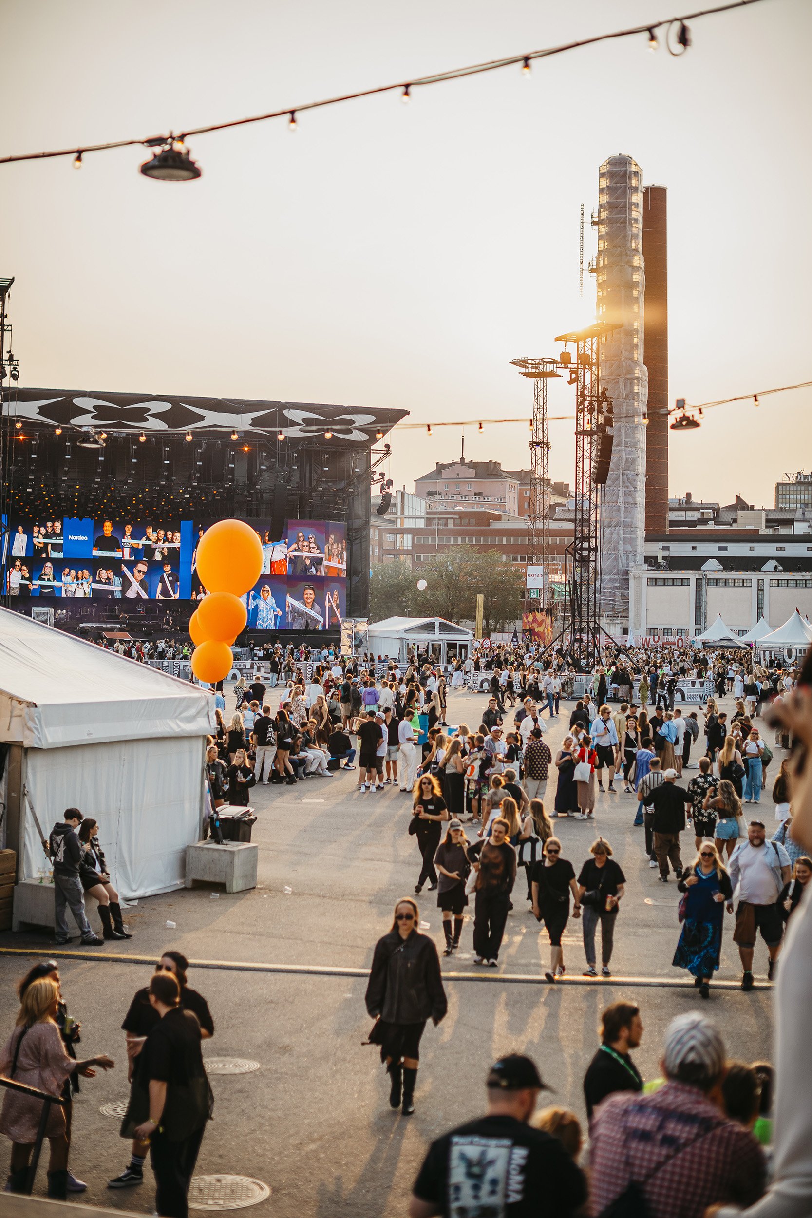 Kuva suuresta tapahtuma-alueesta kesäisenä iltana, jossa on paljon ihmisiä kokoontuneena katsomaan konserttia suurelta lavalta, jonka taustalla näkyy videoseinä.