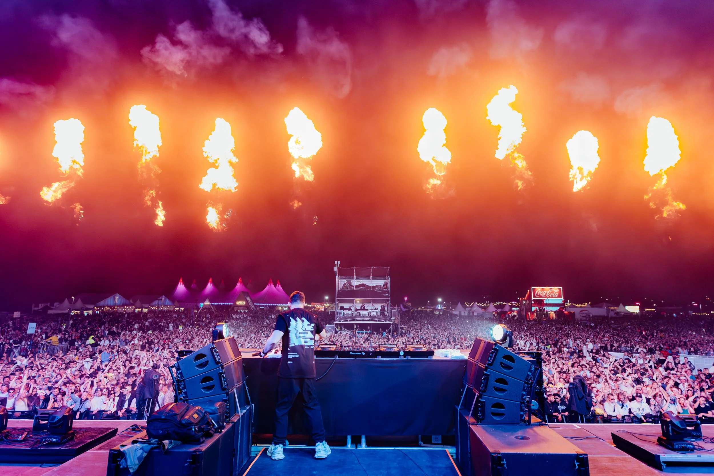 Tapahtumassa esiintyvä DJ ja suuri yleisö festivaalialueella pyrojen upeat liekit taustalla.