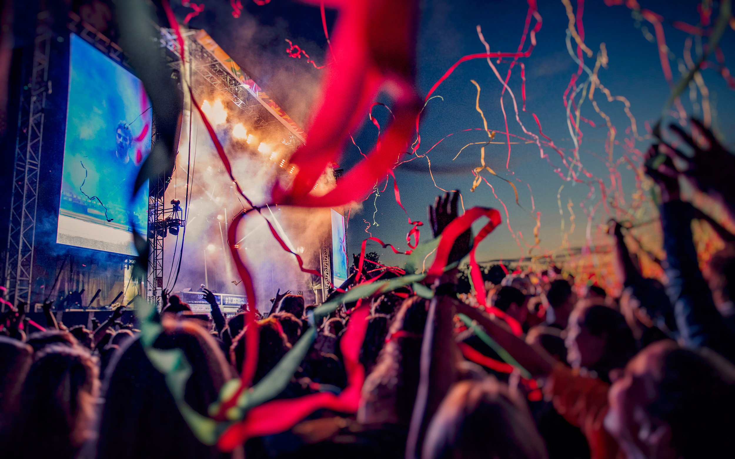 Yleisö juhlii konserttia, jossa on näyttävät konfetit ja valot, ja ilta on sininen taivas taustalla.