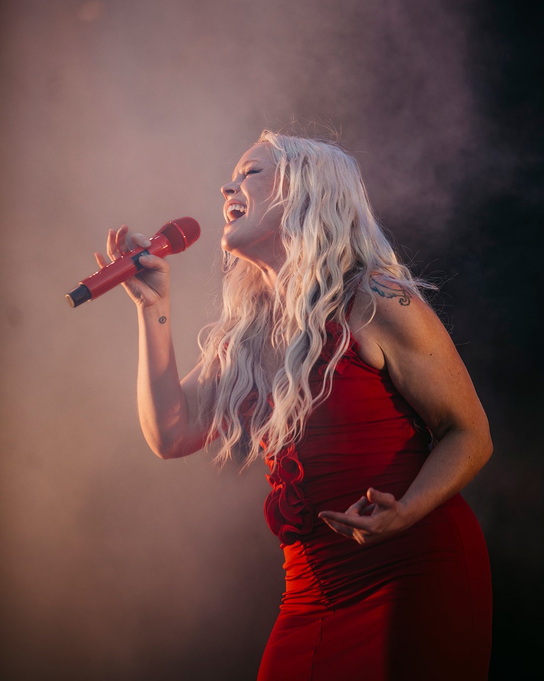 Anna Puu laulamassa mikrofonilla. Hänellä on pitkät vaaleat hiukset ja punainen mekko.