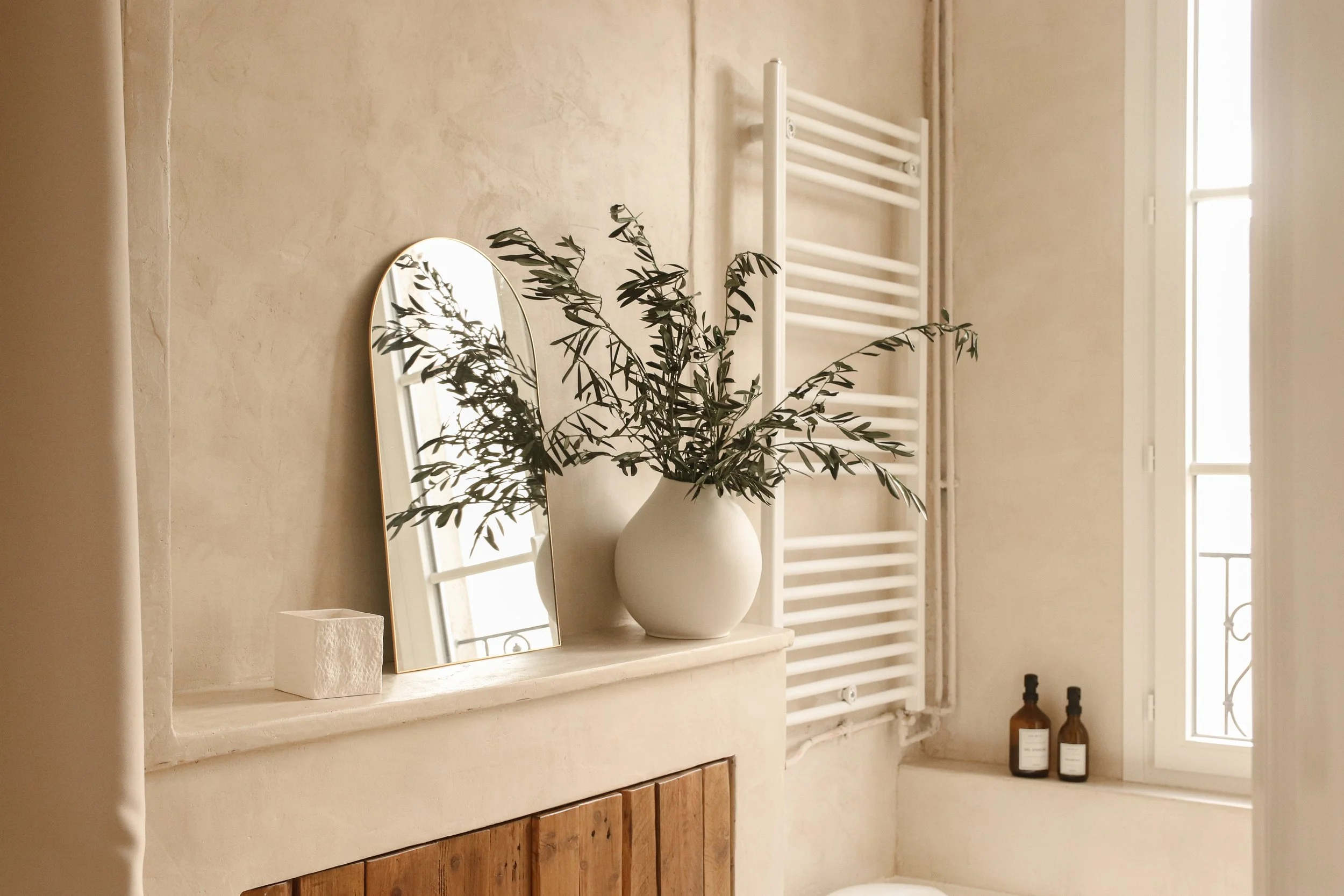 Salle de bain en béton ciré avec portes placard en bois, miroir arche doré, lumière naturelle - ambiance chaleureuse et naturelle