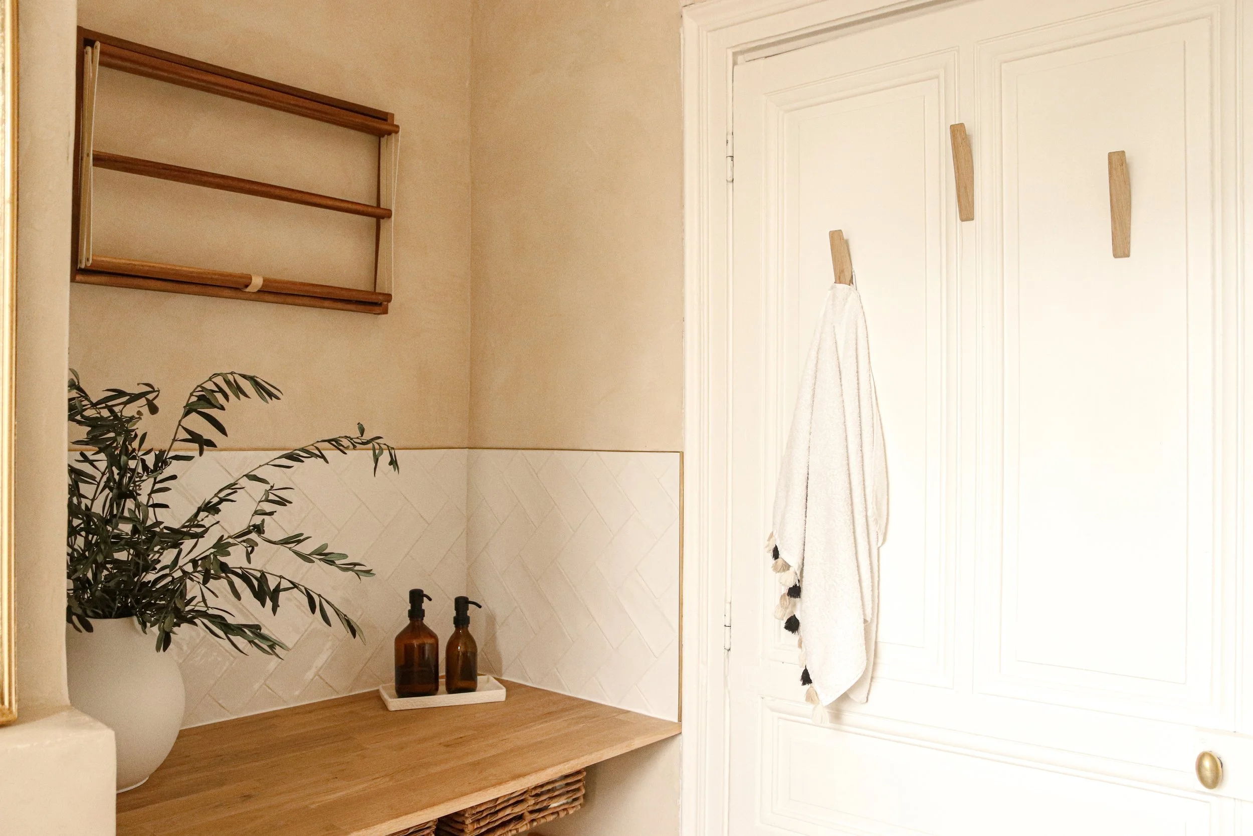Intégration d'un coin buanderie dans une salle de bain en béton ciré avec portes anciennes moulures, avec tablette en bois, panières jute, séchoir mural bois et patère bois - ambiance chaleureuse et naturelle