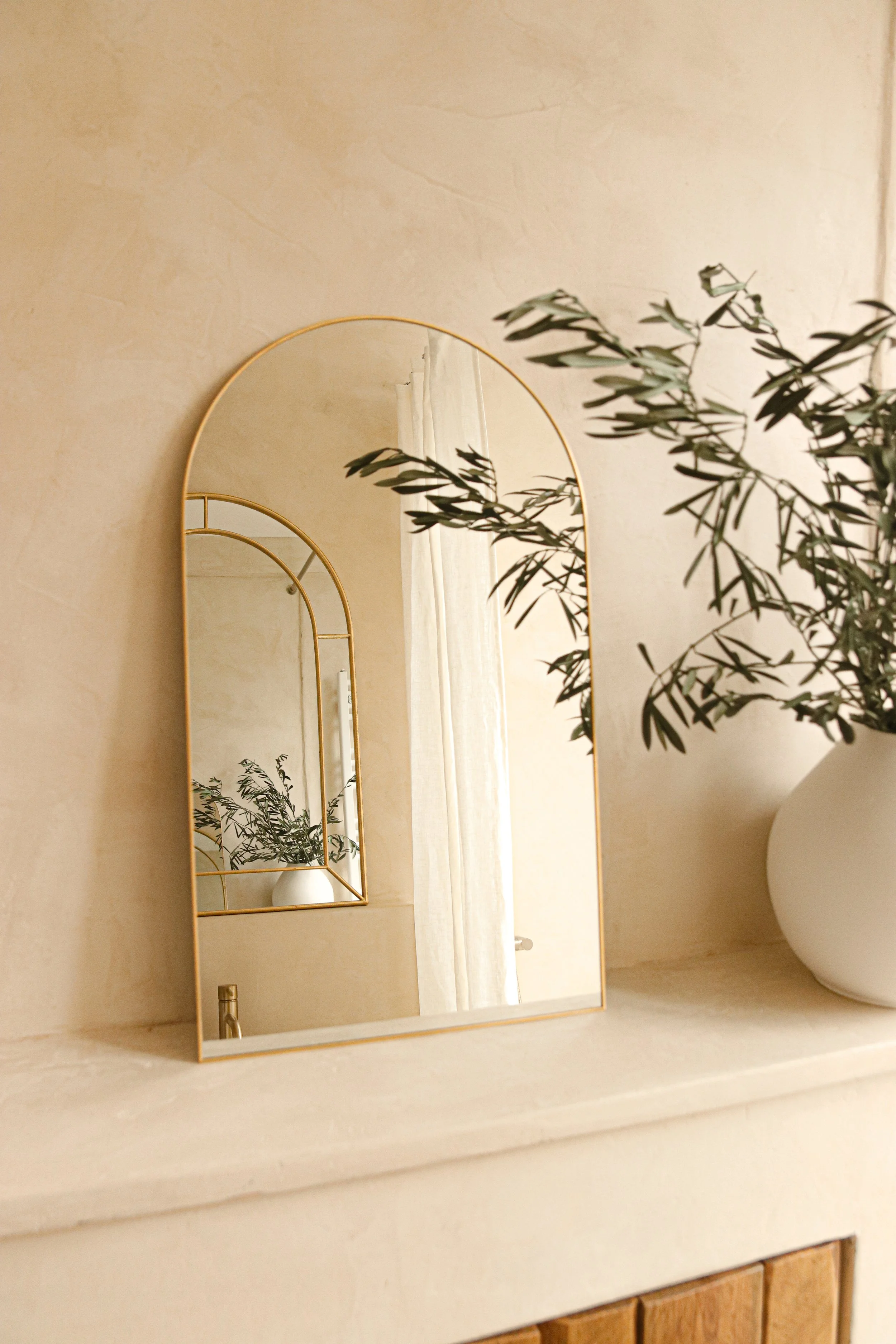 Cheminée en béton ciré avec portes en bois, miroir arche doré - ambiance chaleureuse et naturelle