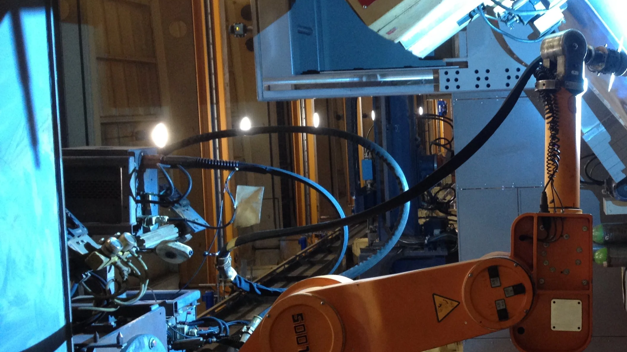 Robotic arm operating in an industrial setting with machinery and equipment around.