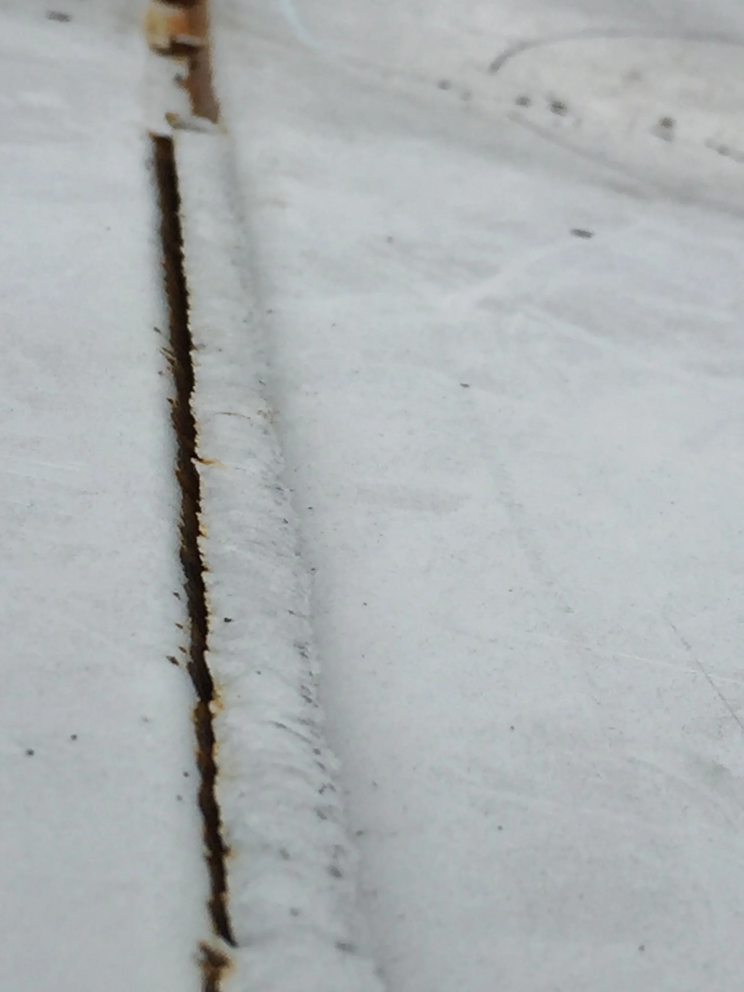 Close-up photo of a small crack or gap along a white painted wall or ceiling.