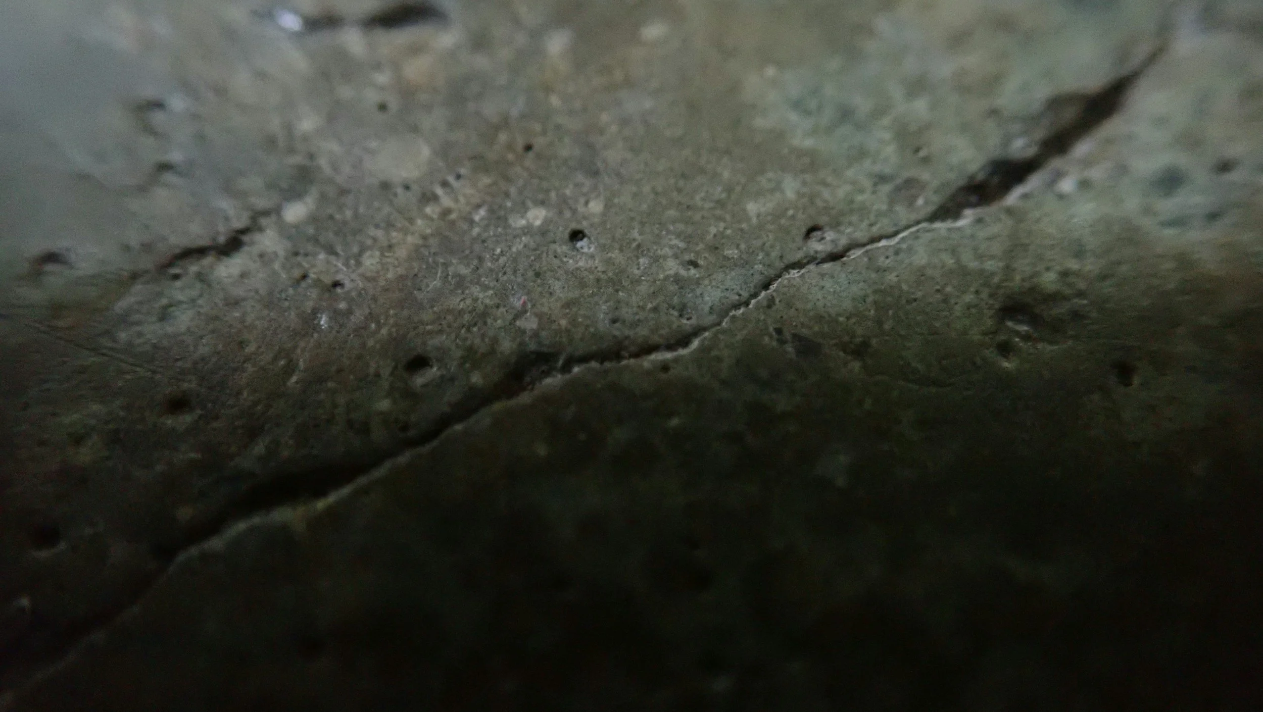 Close-up of a cracked concrete or stone surface with small holes and uneven texture.