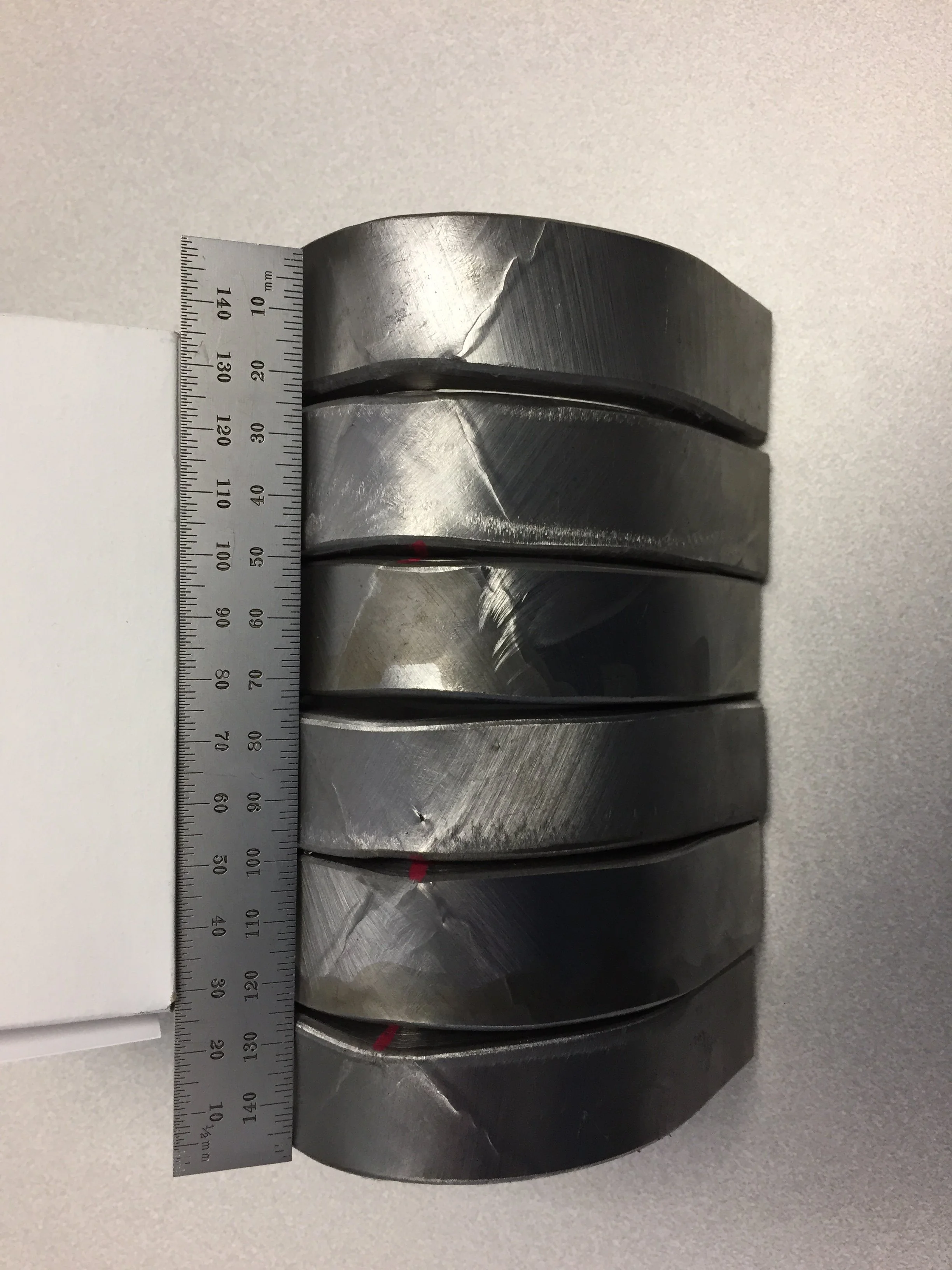 Stack of six metal doughnut-shaped objects with a ruler measuring approximately 150 millimeters placed beside them.