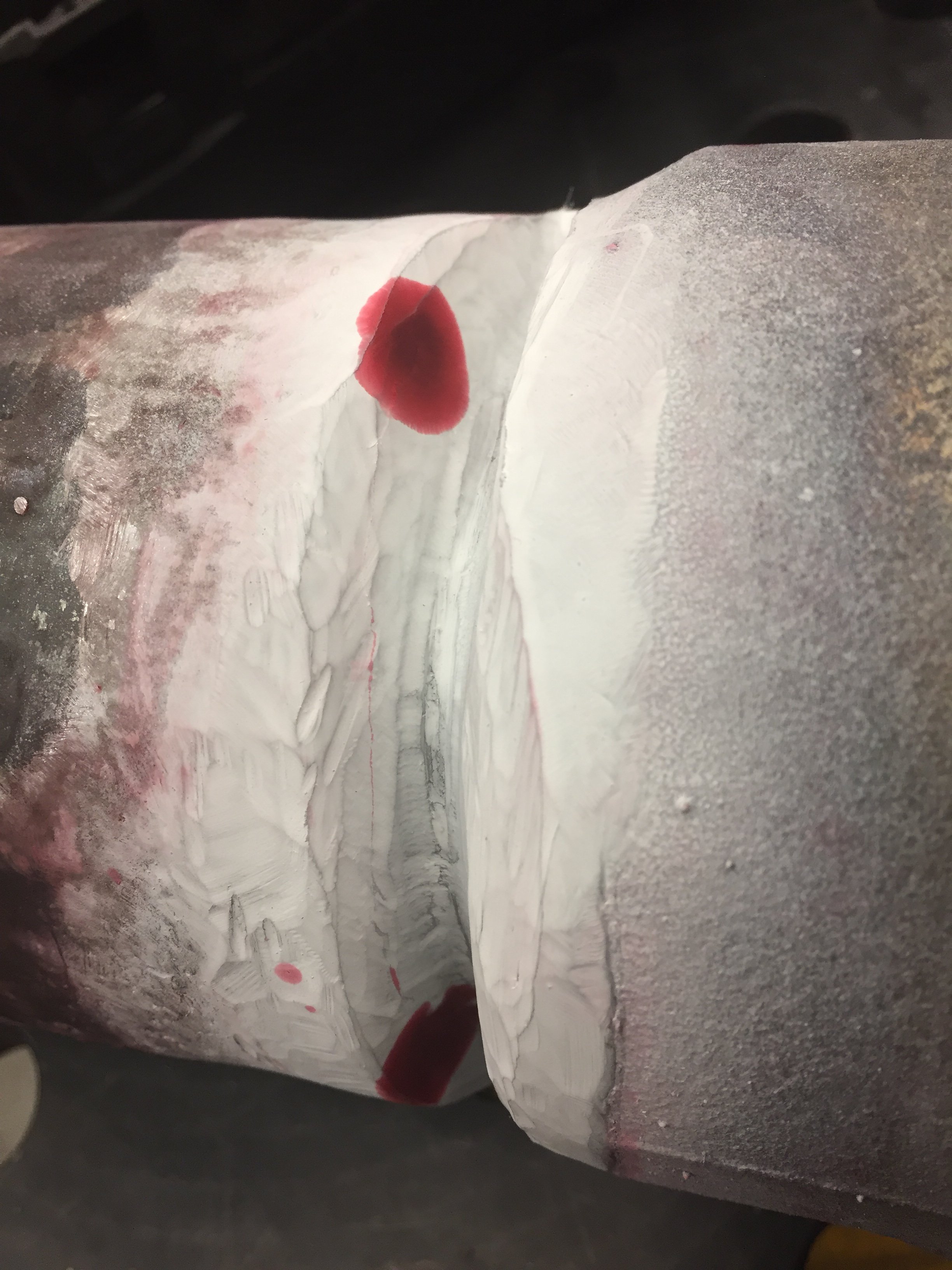 Close-up of a cylindrical object with a rough, textured surface on one side, and white and red paint or substance layered on its surface, with some red spots or stains.