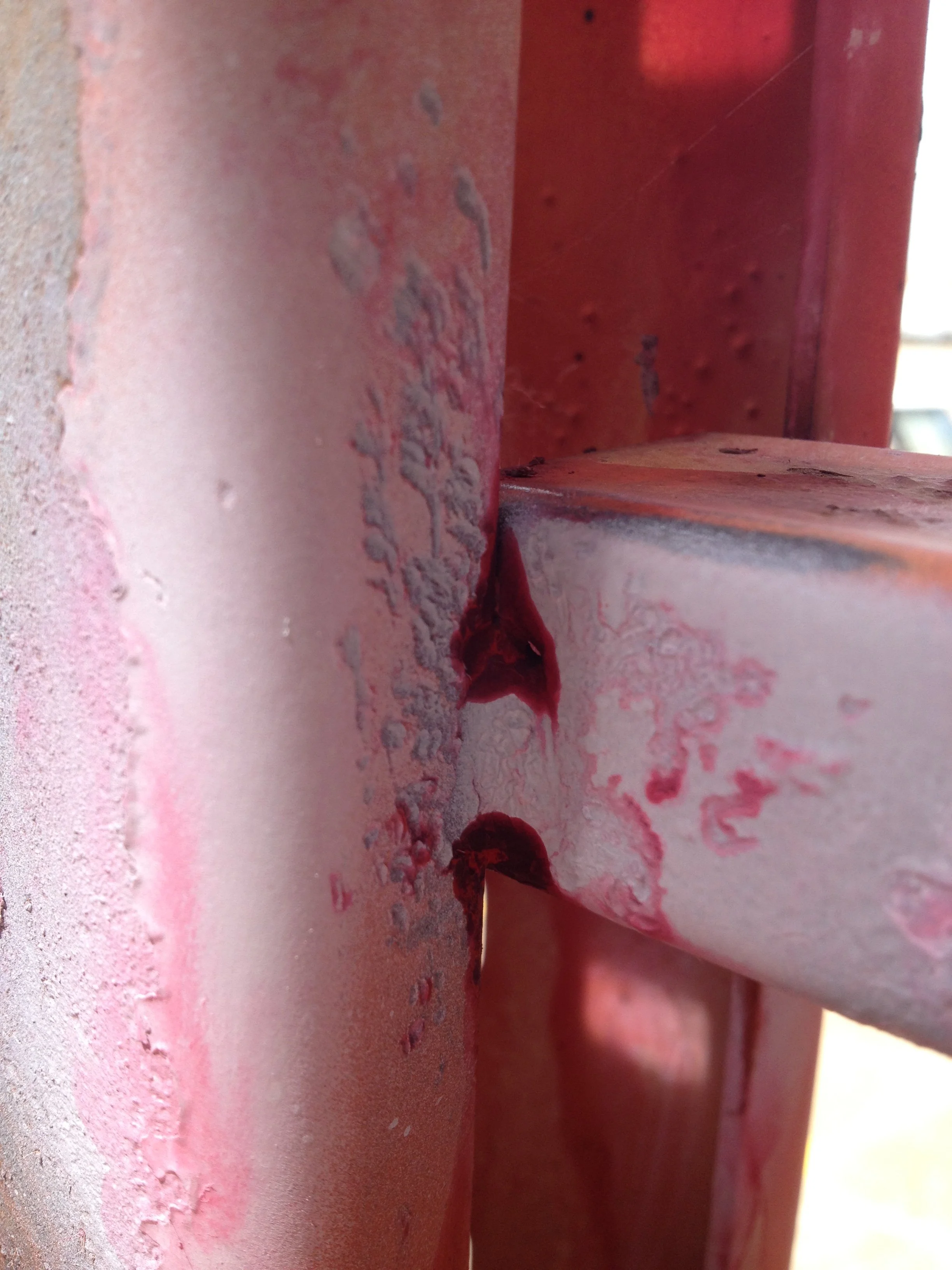 Close-up of a metal structure with chipped red paint and some rust.