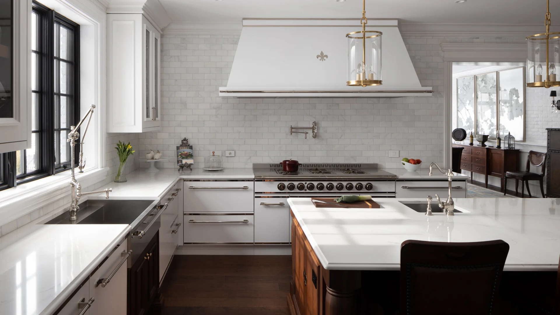 Bright kitchen with white cabinets, black window frames, a white marble countertop island, stainless steel appliances, and a view into a dining room with dark wood furniture.