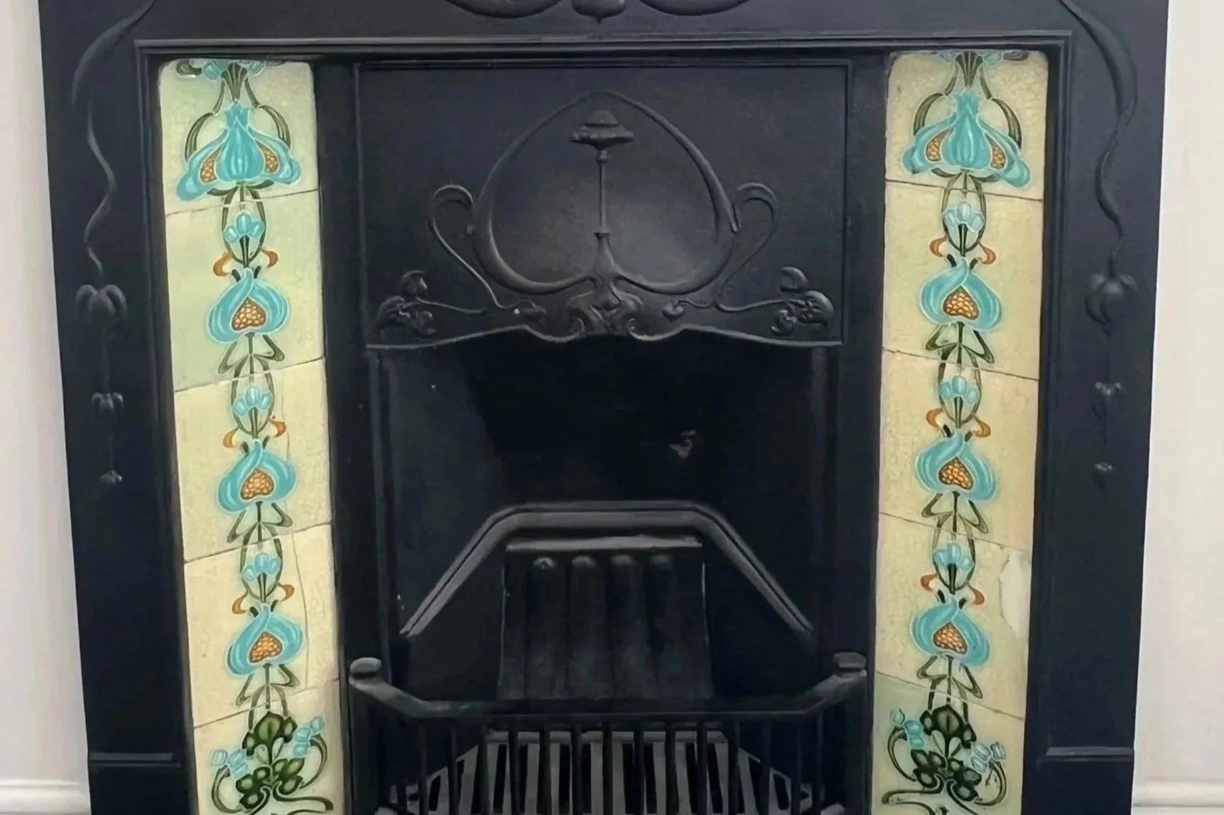 A black cast iron fireplace with decorative blue and yellow floral tiles on the sides.