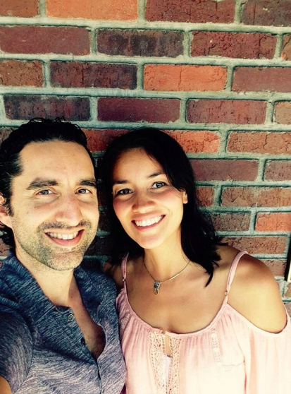 A smiling man and woman taking a selfie together in front of a brick wall.