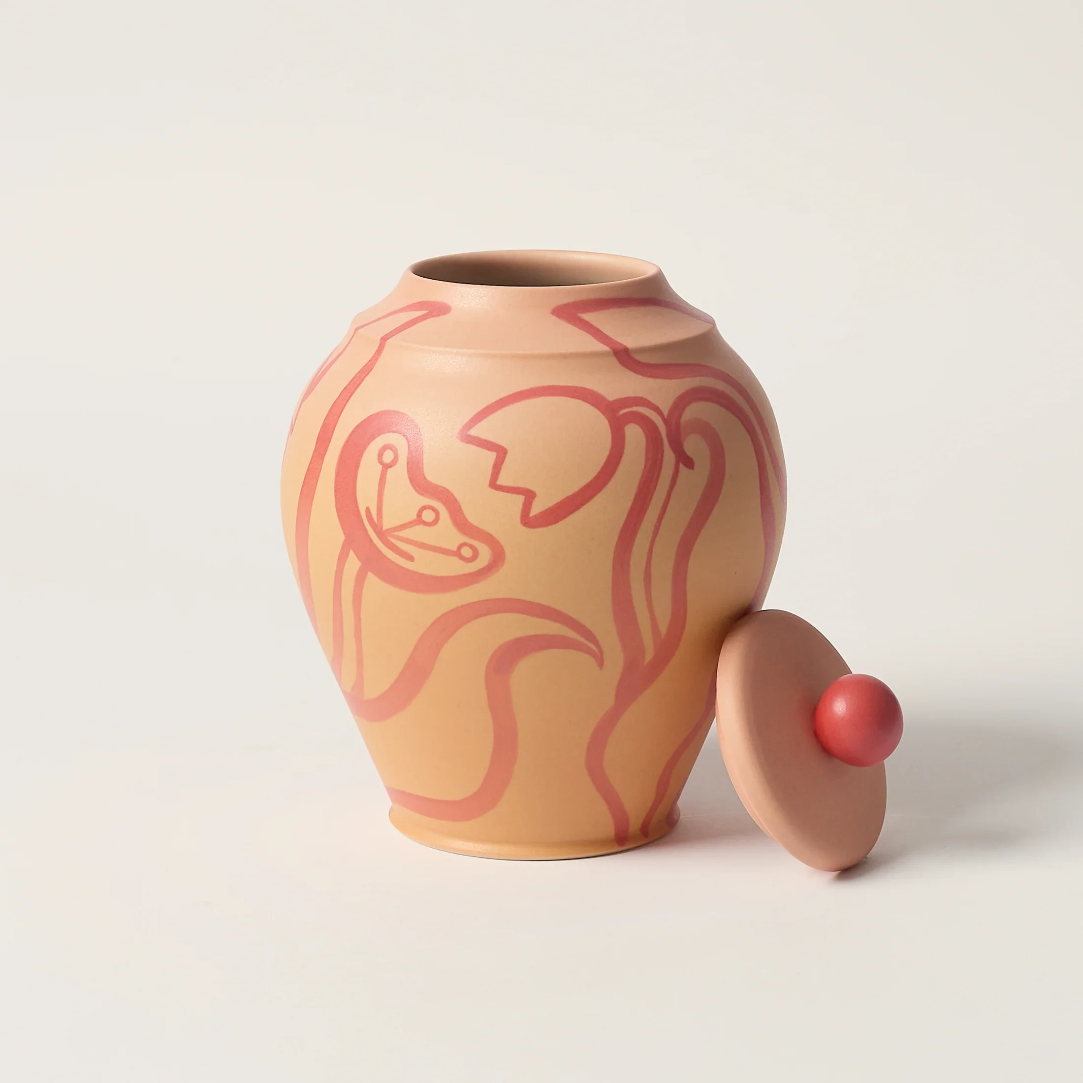 A round ceramic vase with abstract pink line art and a removable lid with a pink knob, placed on a white surface.