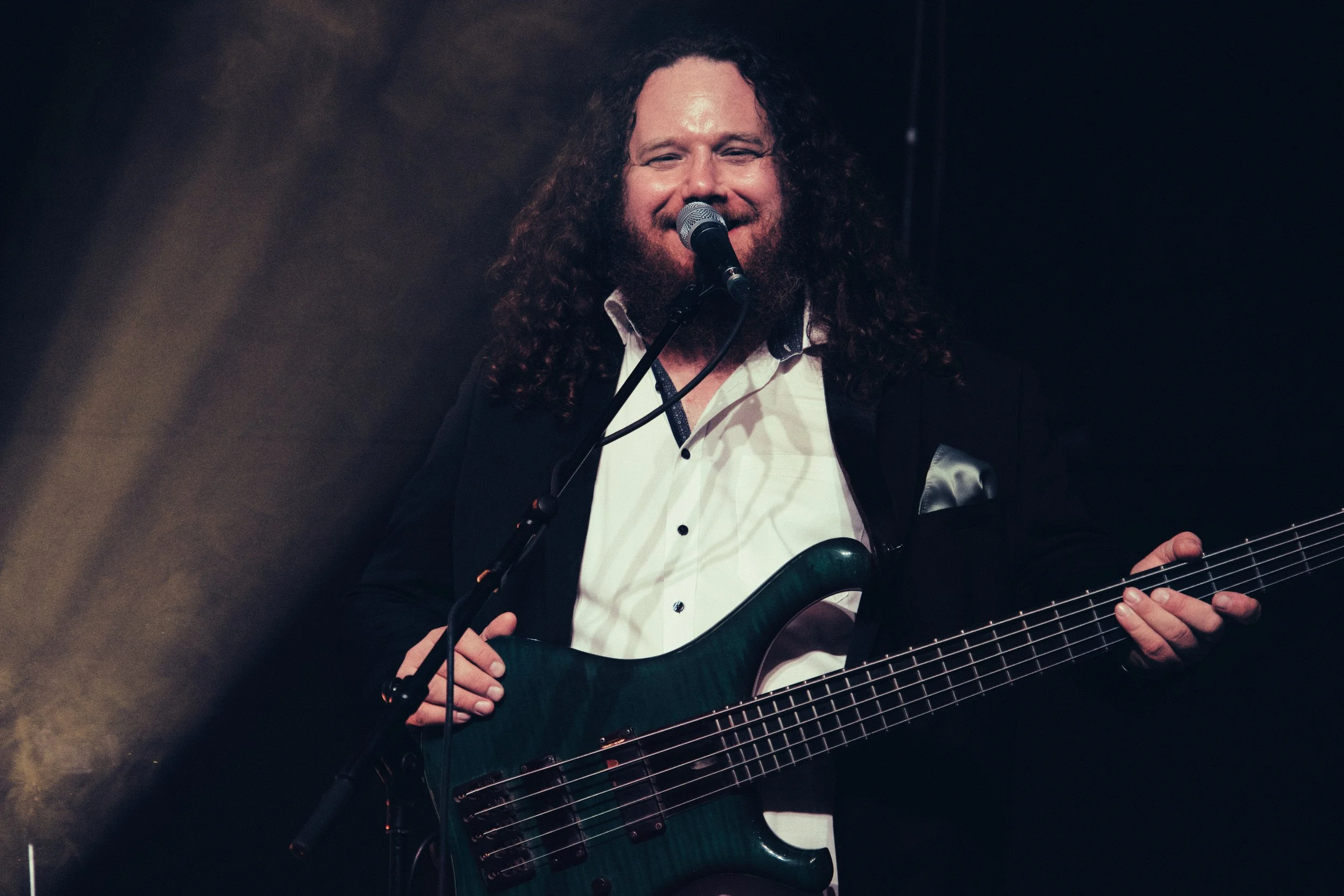 Ein männlicher Musiker mit Langhaar und Vollbart, der auf einer Bühne ein dunkles E-Gitarrenspiel spielt und singt.