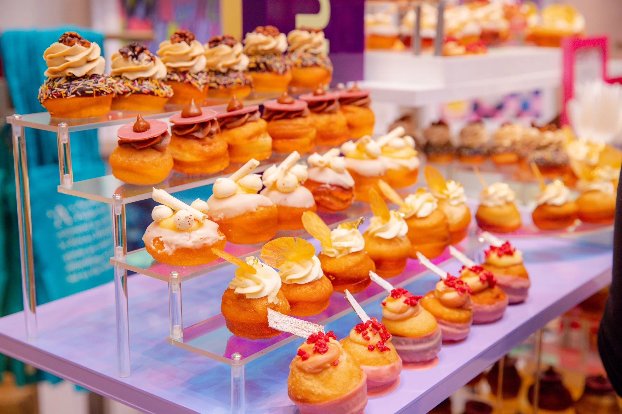 Display of assorted mini donuts with various toppings and glazes on a tiered stand at a bakery or food stall.