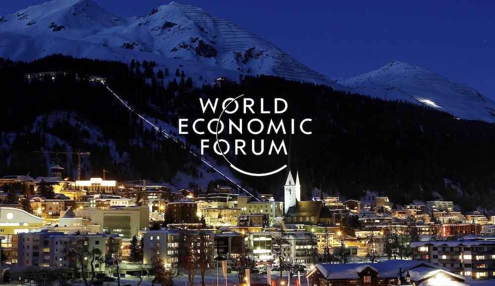 Nighttime view of a snow-covered mountainous city with illuminated buildings and a church with a tall steeple, overlaid with the words 'World Economic Forum'.