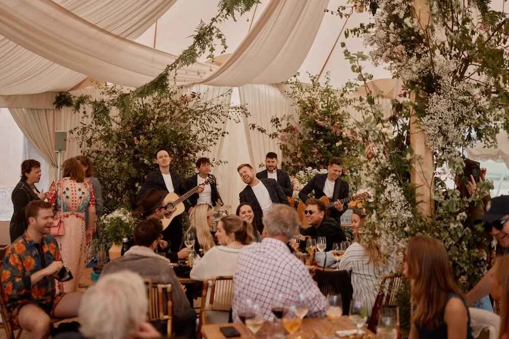 A group of musicians performing at a wedding reception with guests seated at tables.
