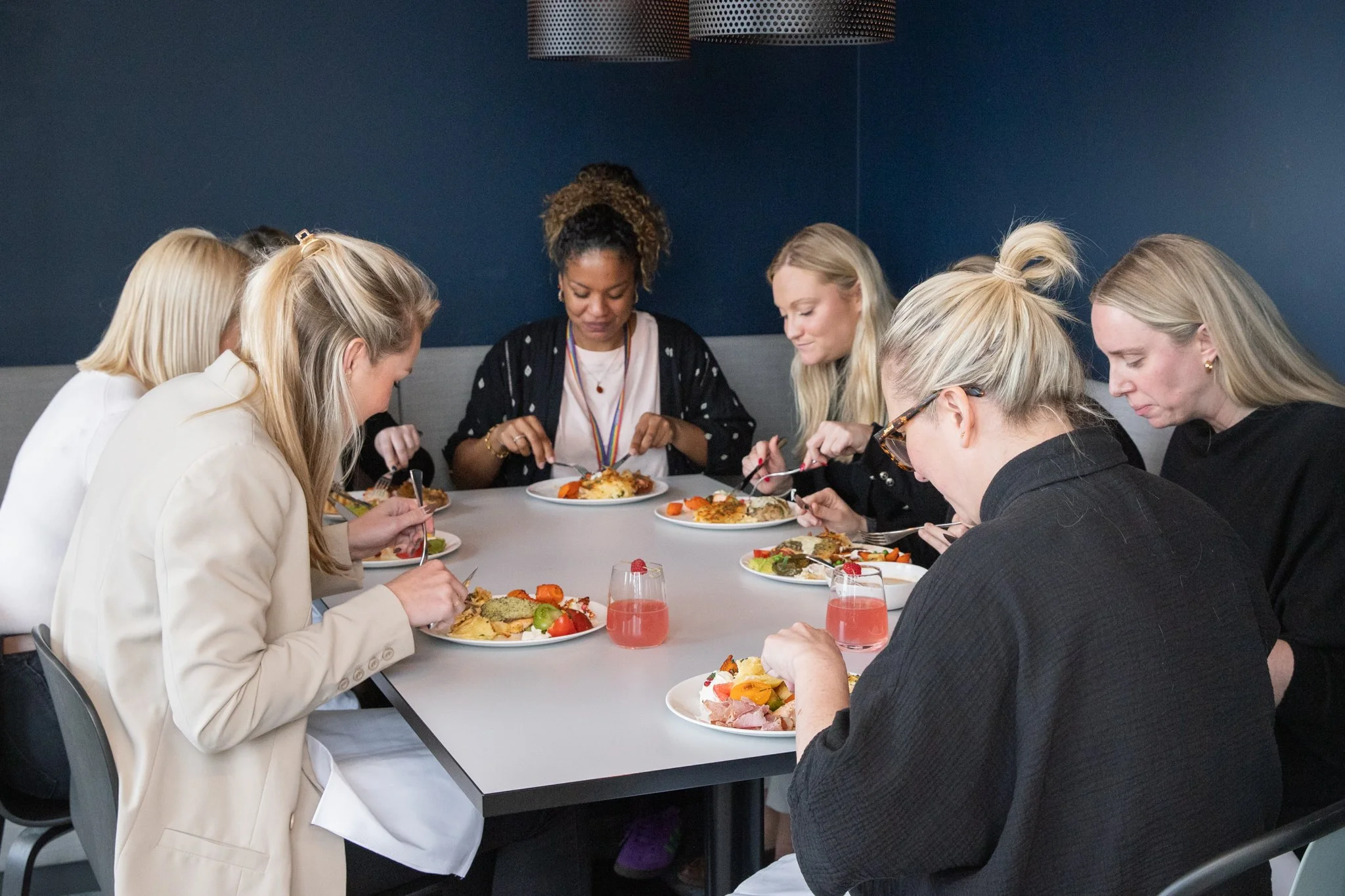 Group of women eating dinner and having drinks at a table in a modern restaurant.