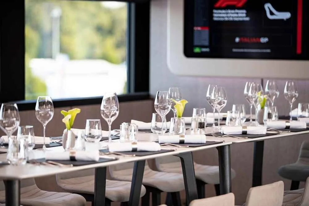 Restaurant table set with wine glasses, water glasses, napkins, and small vases with yellow calla lilies