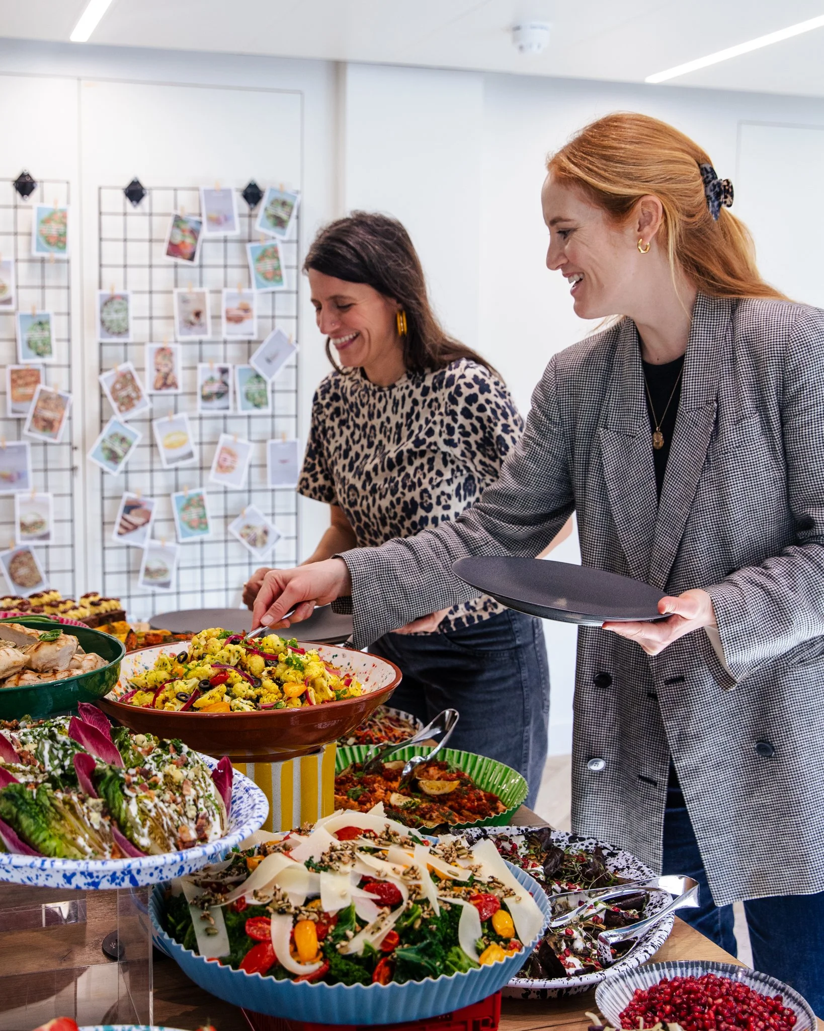 Two women serve themselves at a salad buffet with various colorful salads and dishes on display.