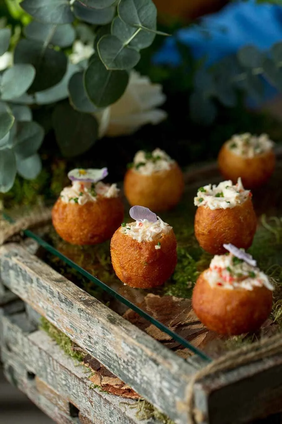 Fried bread bowls filled with creamy seafood salad garnished with edible flowers on a wooden tray.