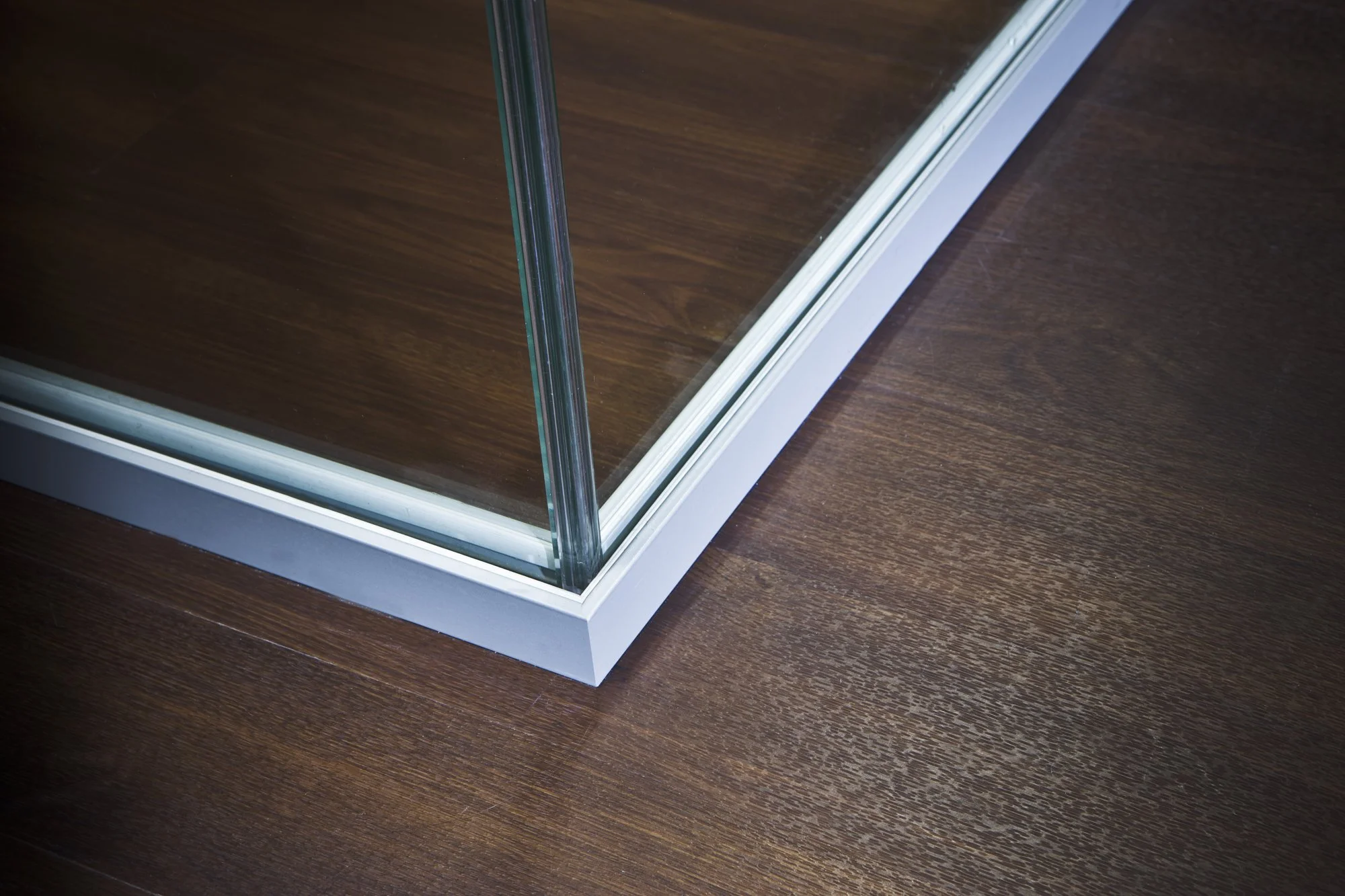 Close-up of the corner of a glass display case with a white base on a wooden surface.