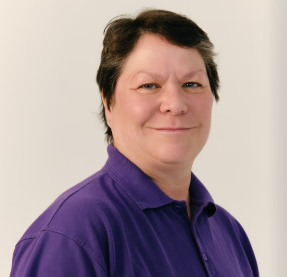 A woman with short dark hair wearing a purple shirt, smiling with a neutral background.