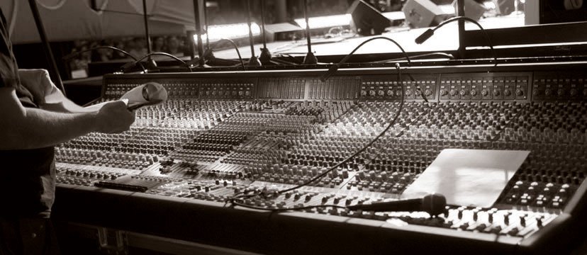 A person adjusting audio equipment on a large sound mixing console in a recording or broadcast studio.