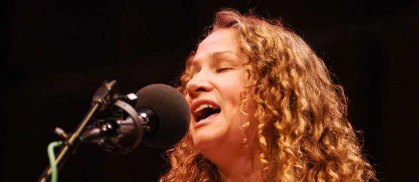 A woman with curly red hair singing into a microphone.