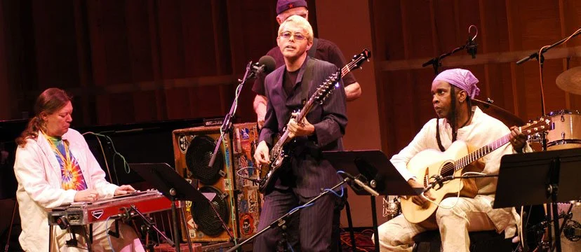 Musicians performing on stage with guitars, keyboard, and drums in a wooden hall