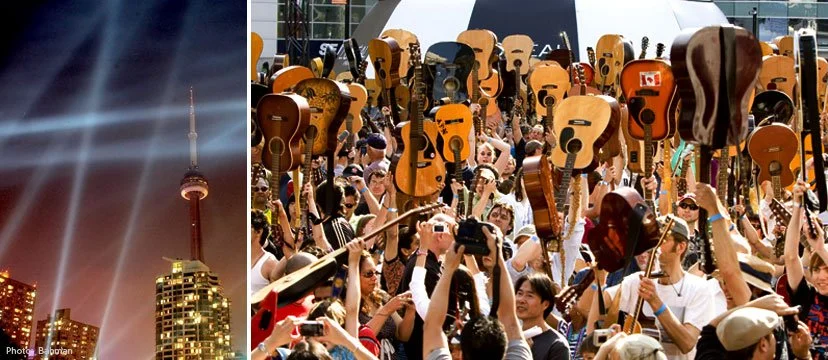 A crowd of people holding up numerous guitars above their heads at an outdoor event.