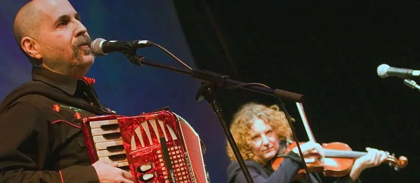 A man playing an accordion and a woman playing a violin on stage during a performance.