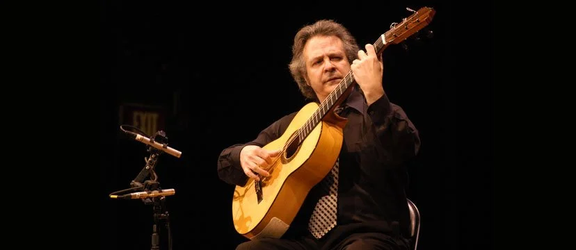 Man sitting and playing an acoustic guitar on stage.