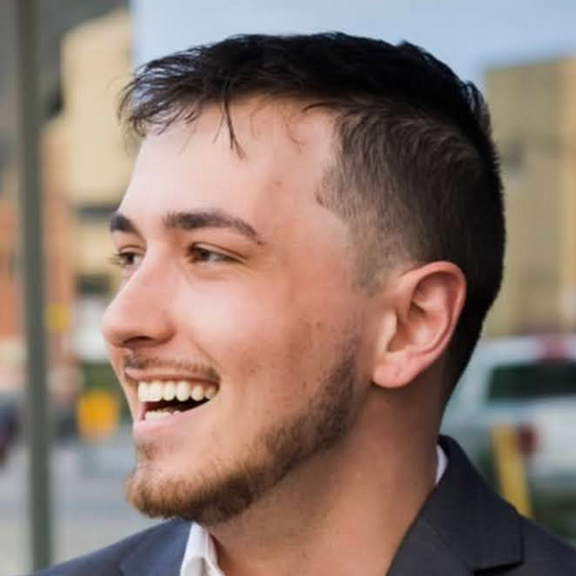 A headshot photo of a man standing in a city addressing a crowd.