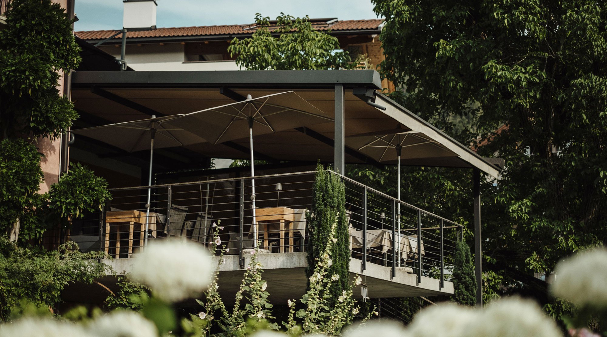Moderne Terrasse mit SonnenSchirmen, die auf einer Balkonkonstruktion im Grünen steht.