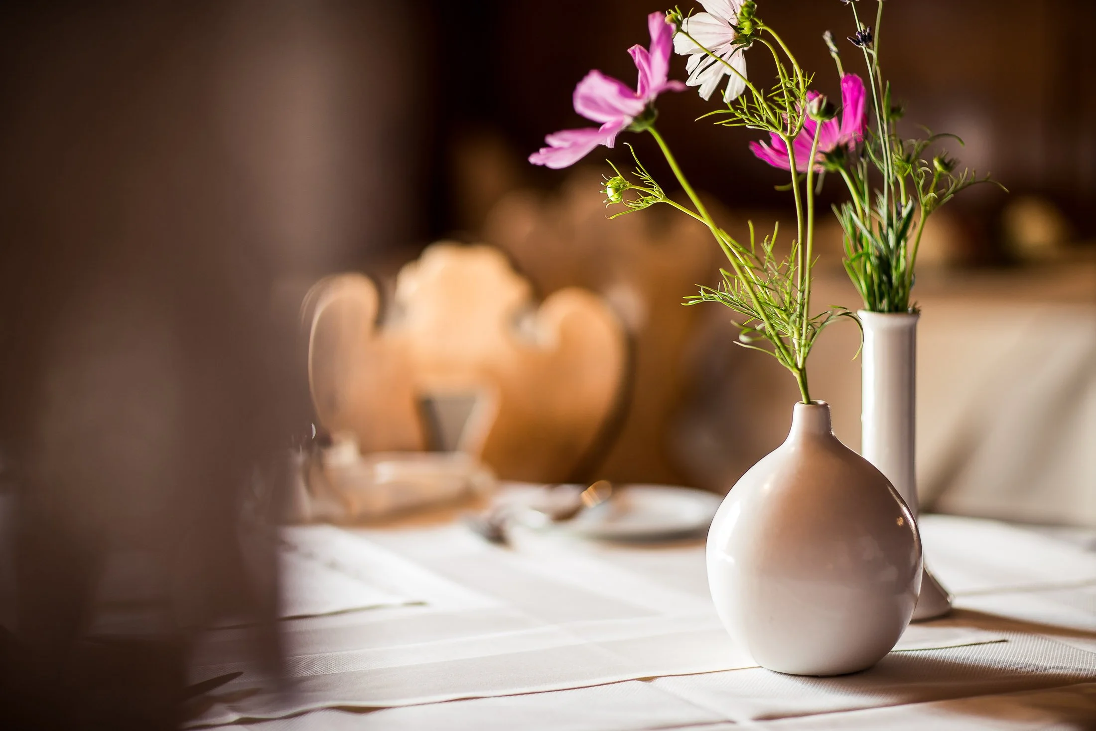 Bunte Blumen in weißen Vasen auf einem Tisch, mit warmem Hintergrundlicht.