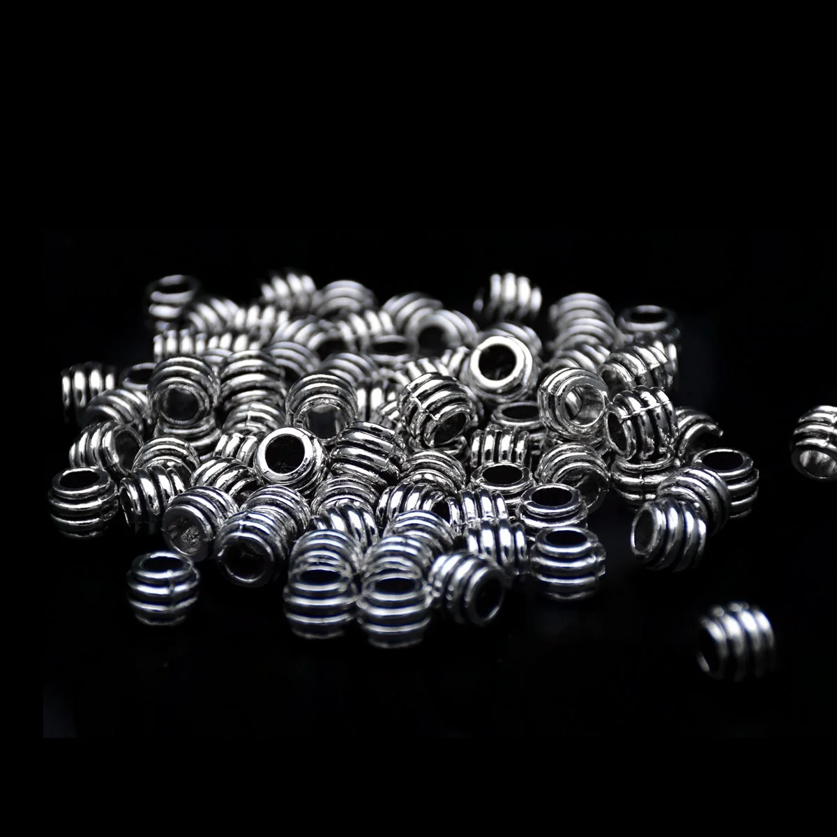 Tibetan silver stripe pattern big hole pandora beads in bulk scattering in a black background