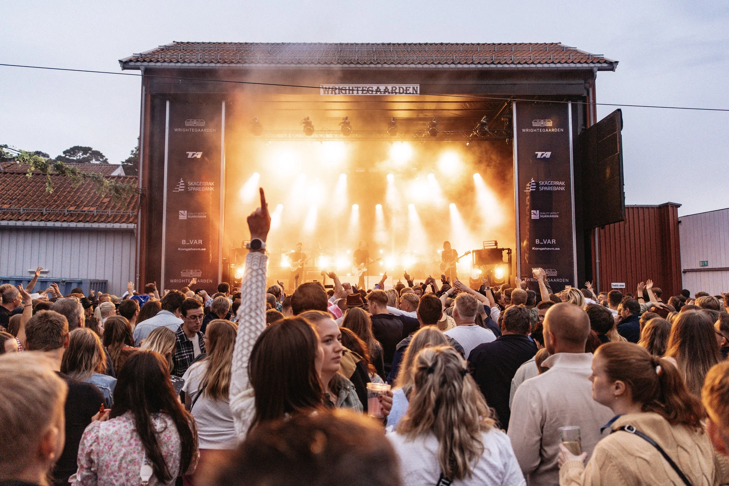 Spectators raising their hands, cheering for the band playing a live concert.