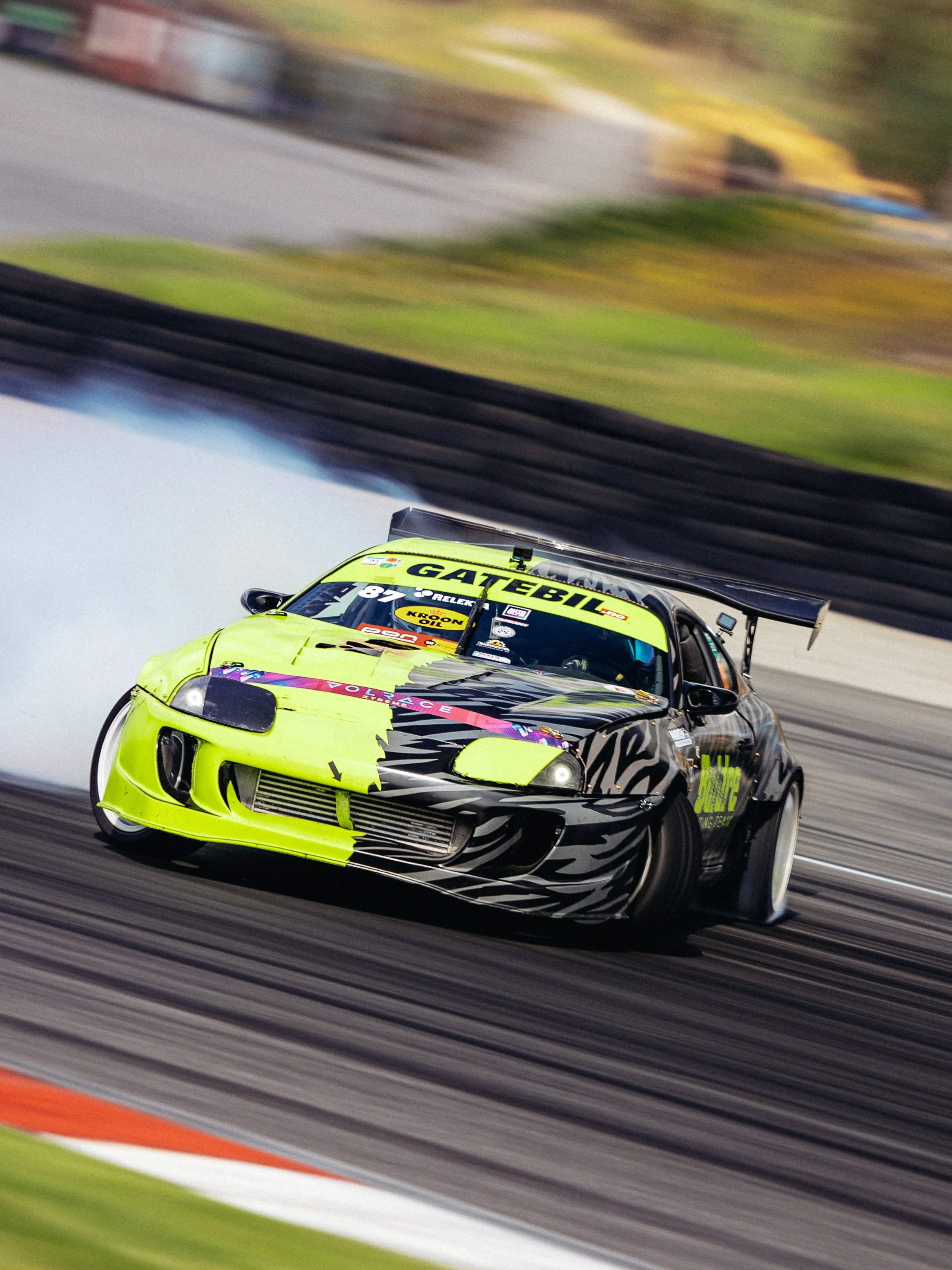 A race car with a neon yellow and black zebra stripe design, fast on a race track with motion blur in the background.